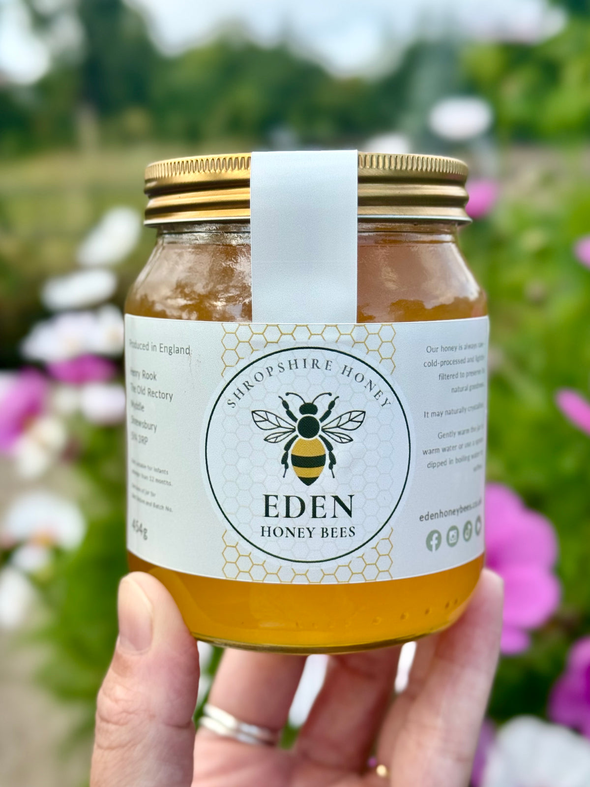 Jar of honey held by a hand with a blurred natural background